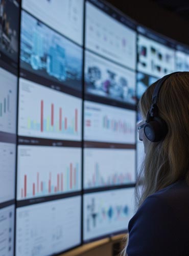 Femme analysant des données sur plusieurs écrans, représentant la veille informationnelle et l’intelligence artificielle.